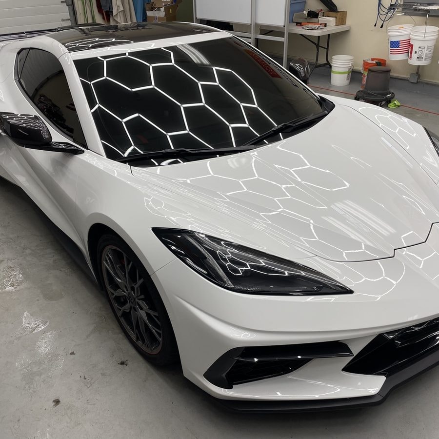 White Chevrolet Corvette C8 with tinted windows, hexagon shop lights reflecting on the glass, at Lindsay Window Tinting in Rochester, NY
