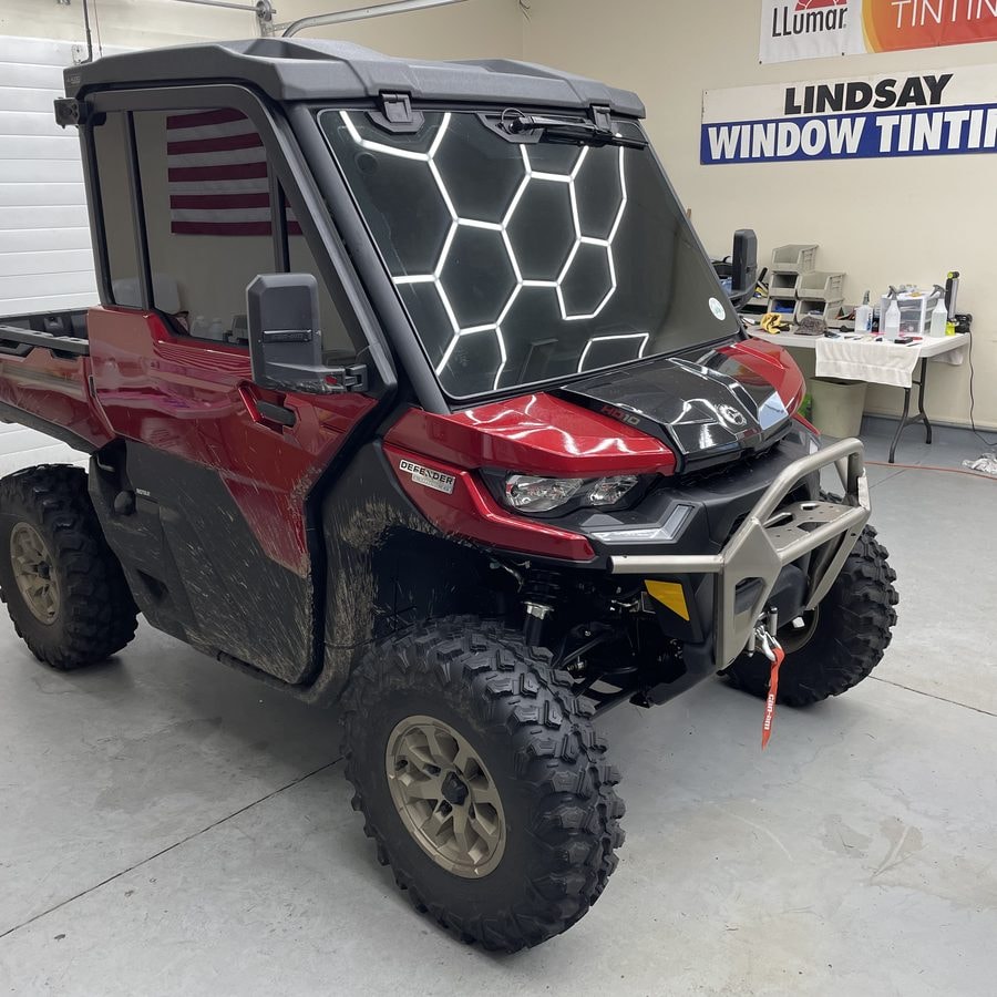 Red Can-Am Defender side-by-side with a tinted windshield inside the Lindsay Window Tinting shop in Rochester, NY