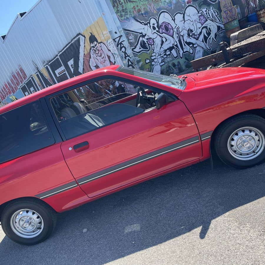 Red Ford Festiva with tinted windows parked beside a graffiti mural wall
