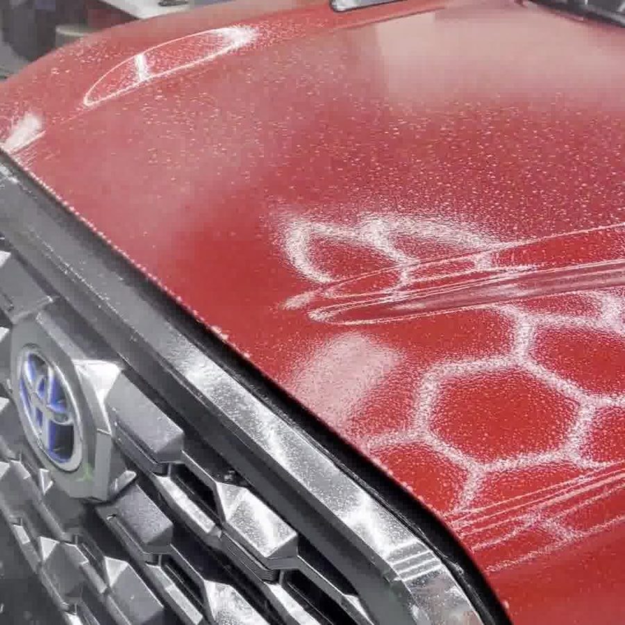 Red Toyota truck hood during a paint protection film install, with hexagon shop lights reflecting on the wet film