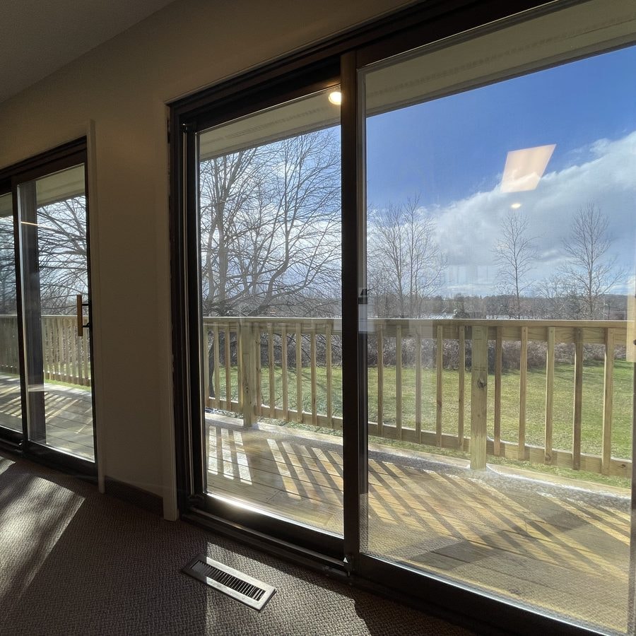 Tinted sliding glass doors in a home, looking out to a deck and trees