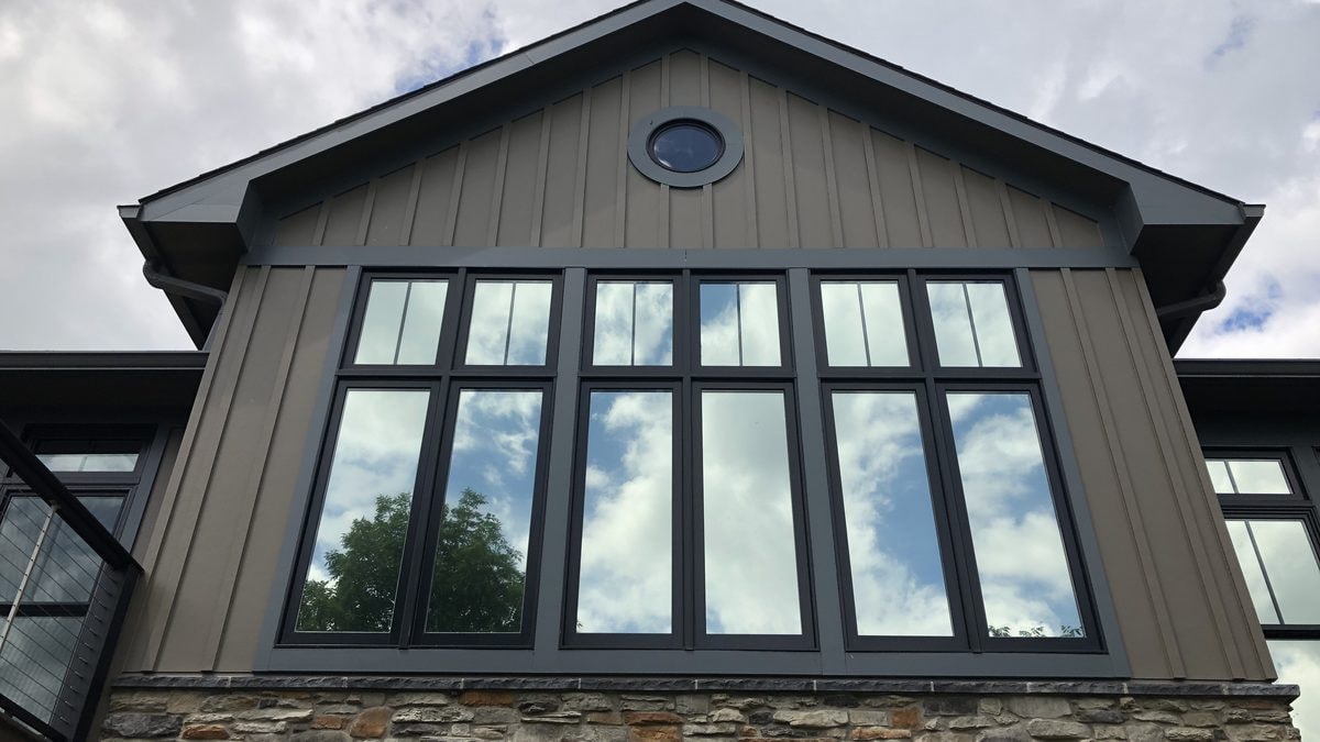 Black-frame home windows with residential window film on a stone and board-and-batten house
